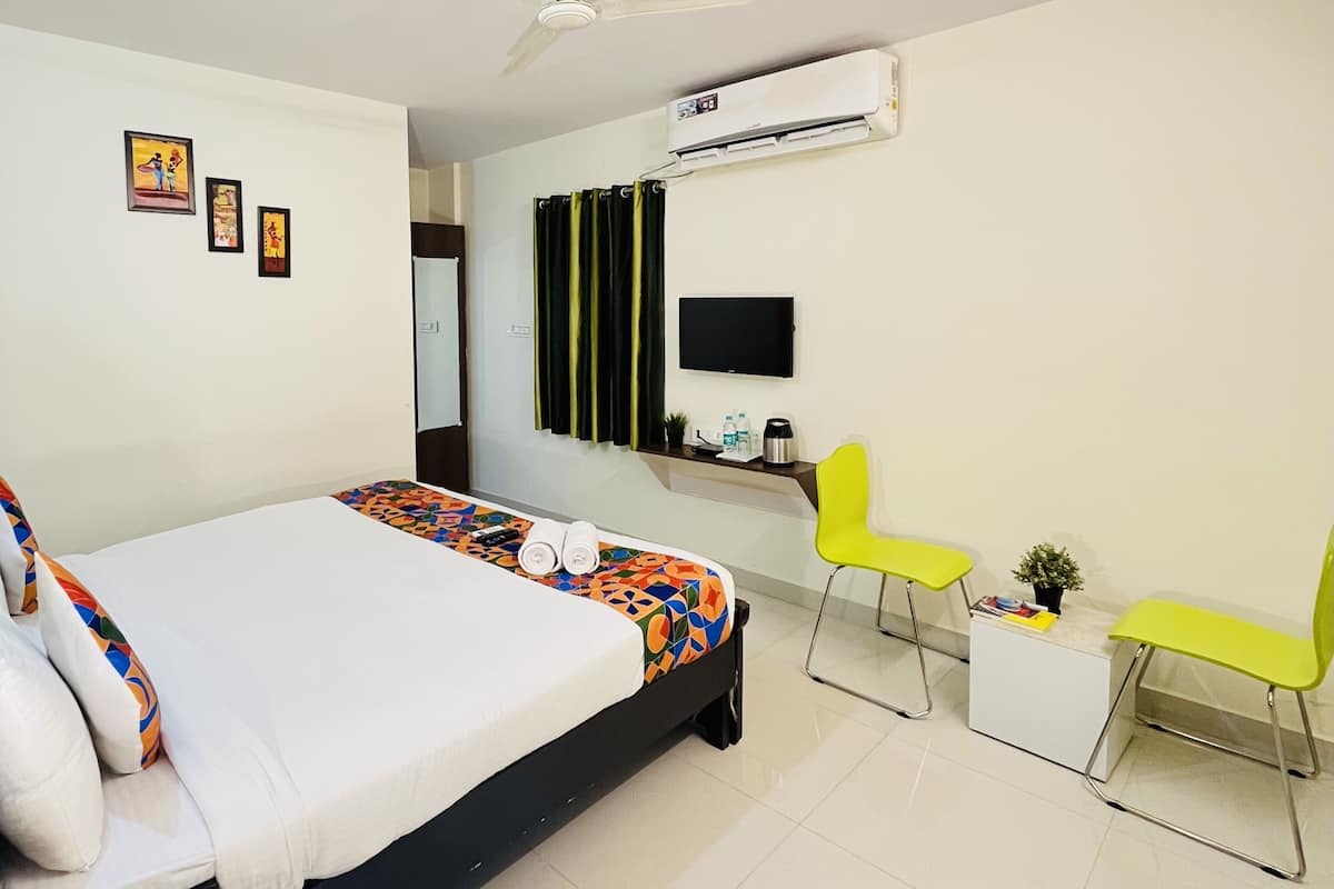 A hotel room with a bed, two chairs, a TV, and an air conditioner.