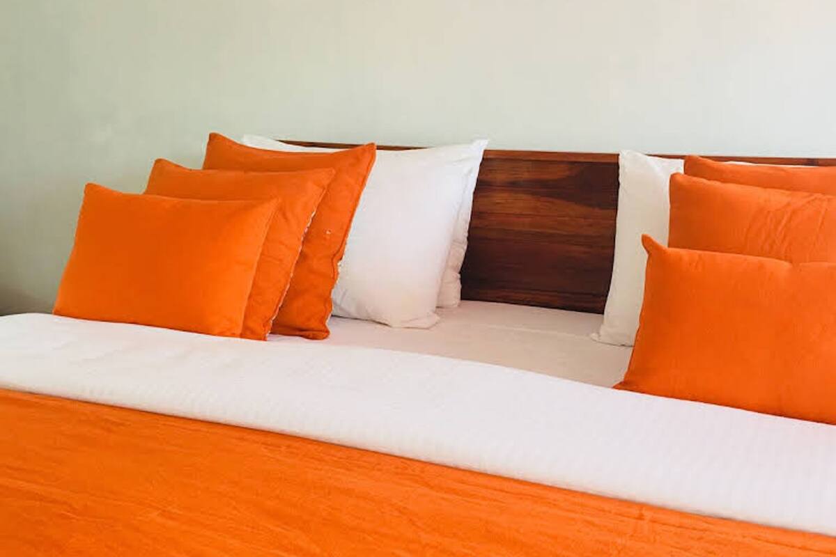 A bed with an orange bedspread and pillows, a wooden headboard, and a white pillow.