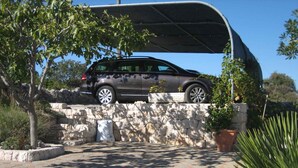 A car parked under a covered area, a stone wall, and a paved driveway with plants. - Villa with air conditioning, terrace and outdoor pool (Rogoznica)