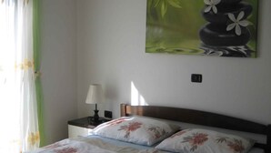 A hotel room with two beds, a nightstand with a lamp, a painting of a stone arrangement, and a window with curtains. - Villa with air conditioning, terrace and outdoor pool (Rogoznica)