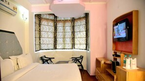 Ein Hotelzimmer mit einem großen Bett, einem Schreibtisch mit zwei Stühlen, einem Fernseher auf einem Holzboden und einem Fenster mit gemusterten Vorhängen.