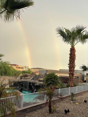 Ein Poolbereich mit Wasserfall, Palmen und einem Regenbogen im Hintergrund.