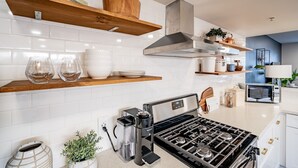 Een moderne keuken met witte tegels, houten planken, een gasfornuis, een koffiezetapparaat en een magnetron.