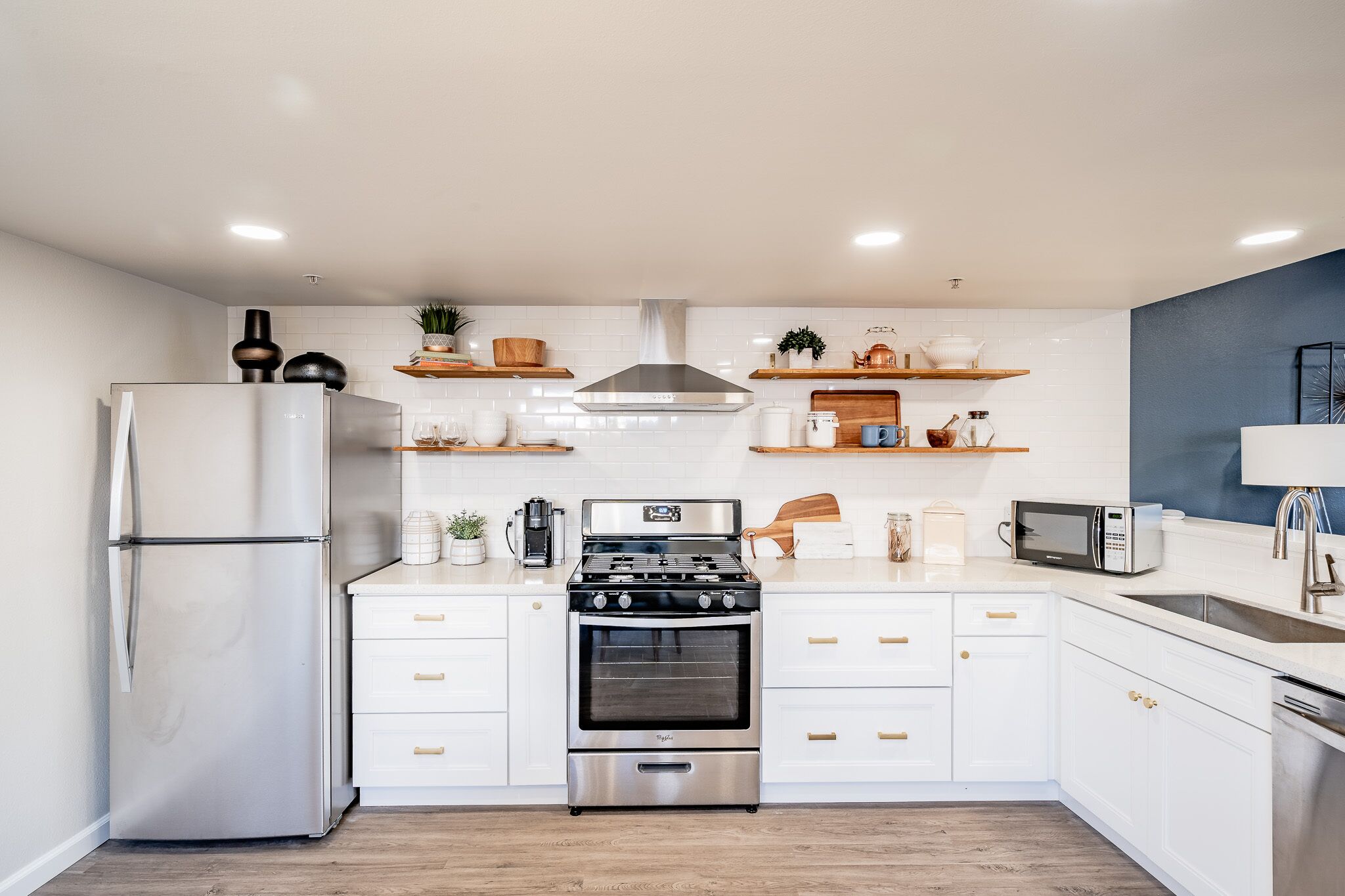 Una cocina moderna con armarios blancos, un refrigerador de acero inoxidable, una estufa a gas y un horno empotrado.