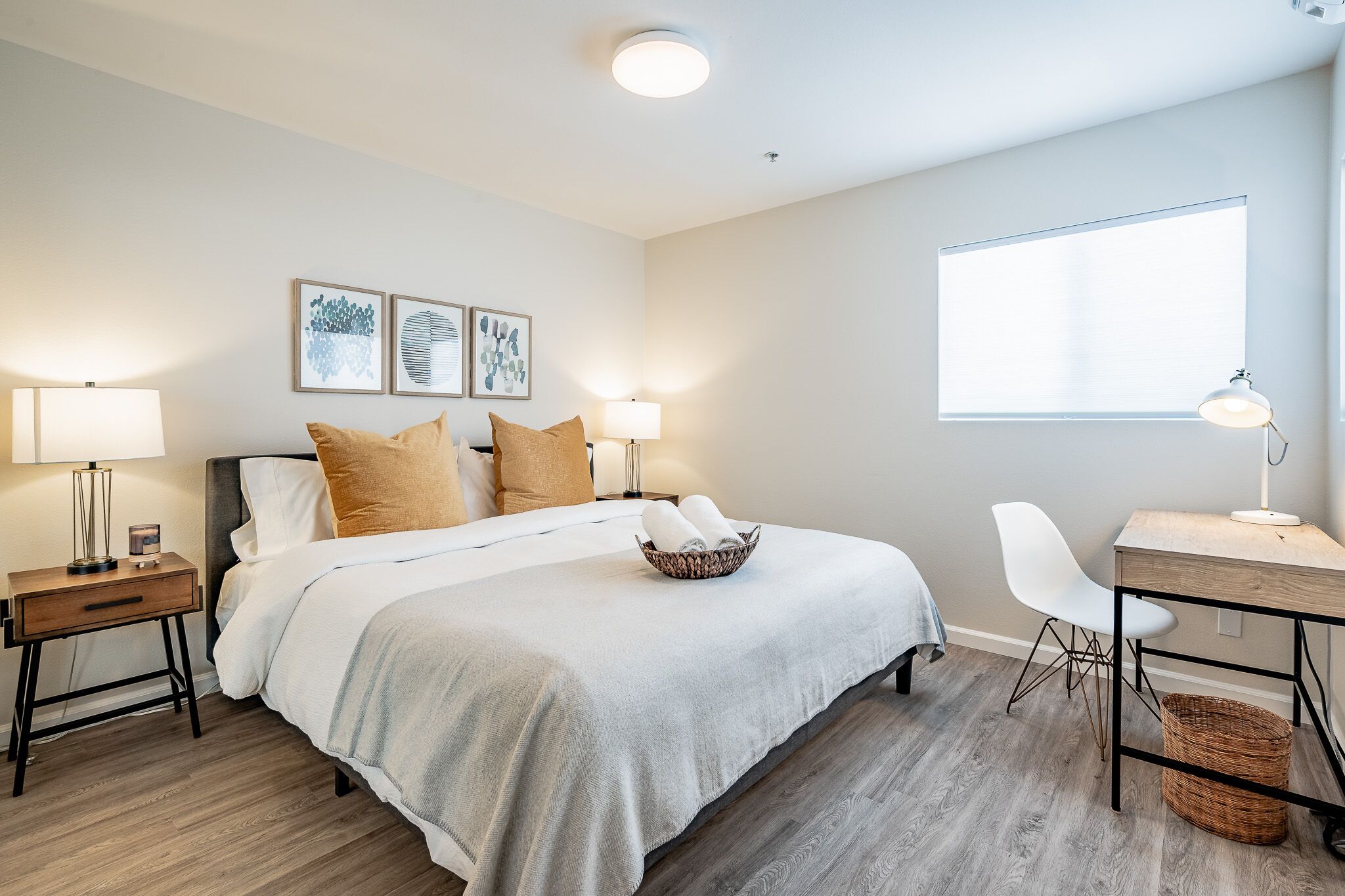 A neatly arranged bedroom with a bed, bedside tables, a desk, and a large window.