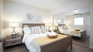 Een slaapkamer met een groot bed, twee nachtkastjes met lampen, een spiegel en kunst aan de muur.