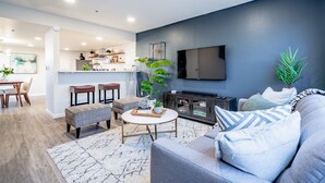 Een moderne woonkamer met een grijze bank, een salontafel en een aan de muur bevestigde televisie.