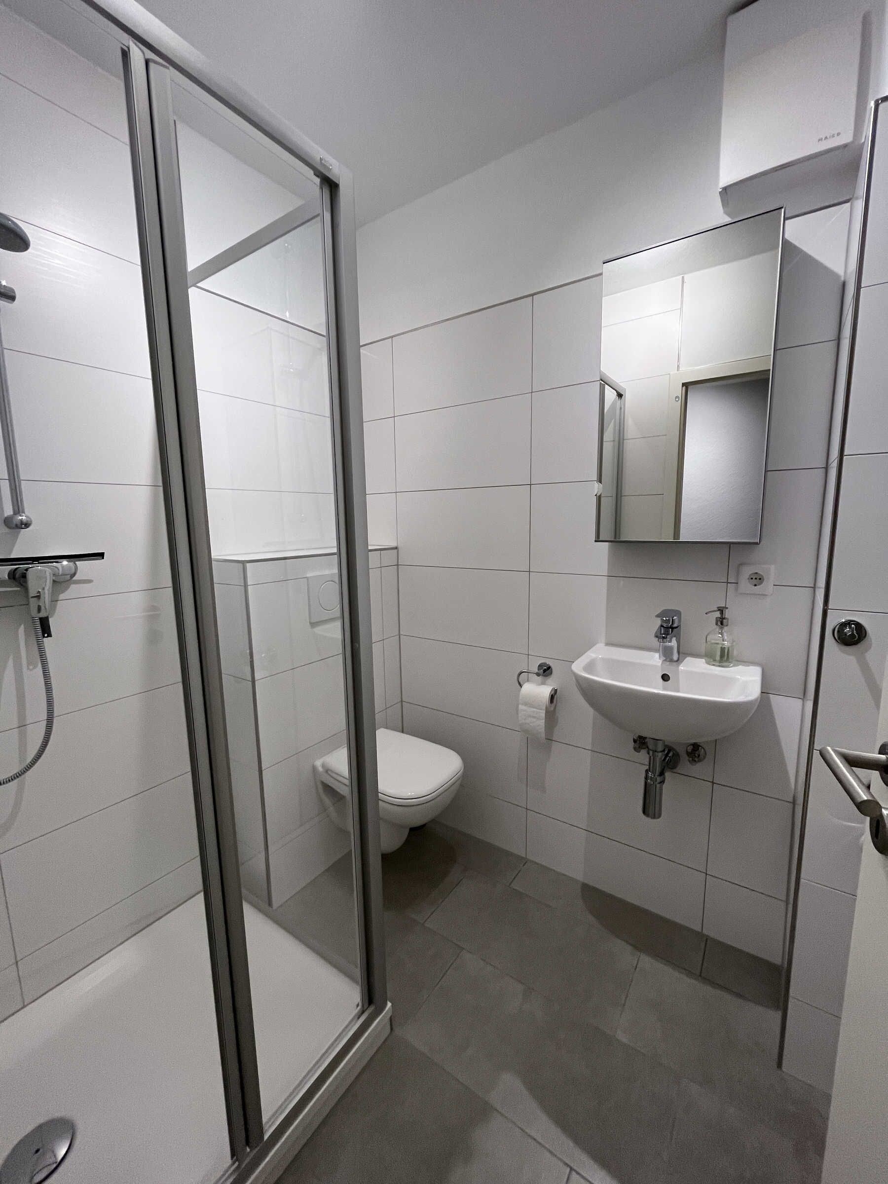 Un bany modern amb plat de dutxa de vidre, vàter i un lavabo amb mirall a sobre.