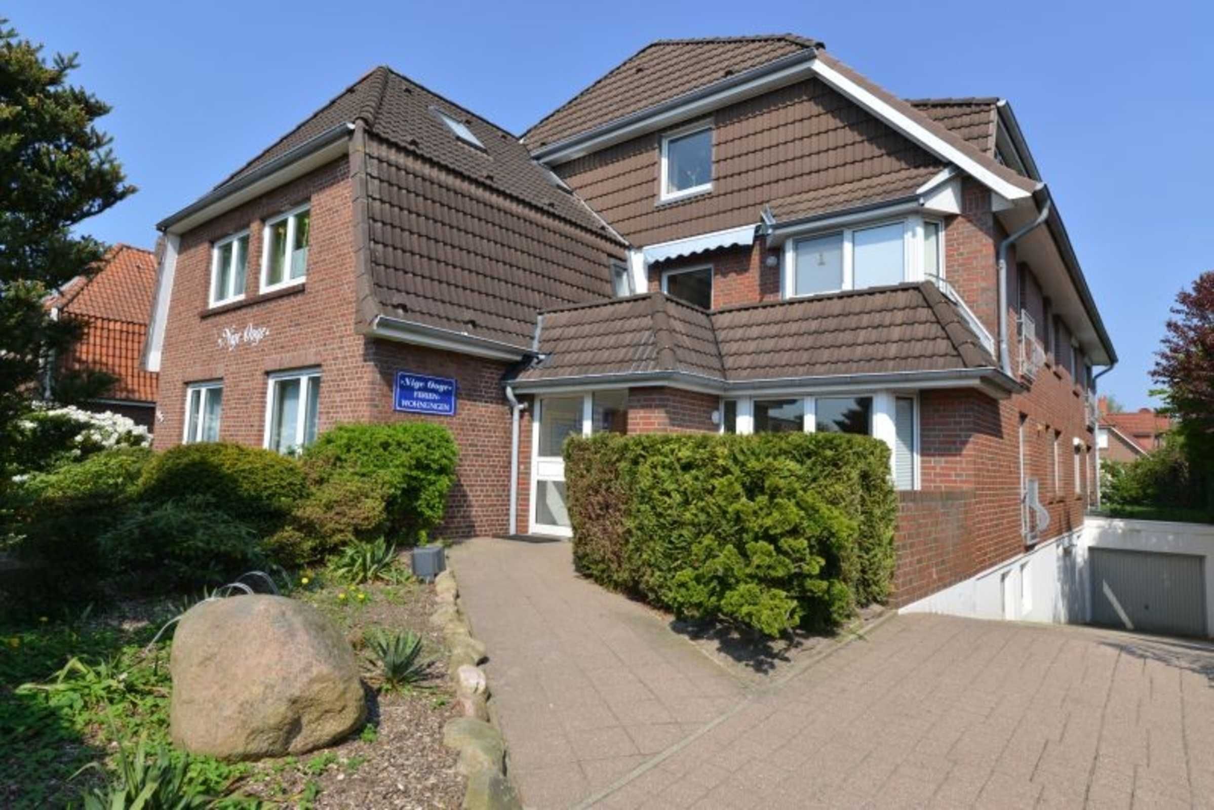 A two-story residential building with a brick facade, a tiled roof, and a well-maintained garden with a large rock and shrubs.