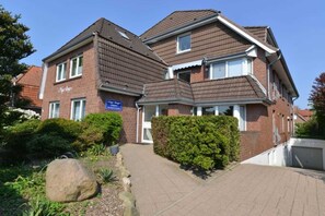 A two-story residential building with a brick facade, a tiled roof, and a well-maintained garden with a large rock and shrubs. - Apartment house Nige Ooge Apartment No. 1 - Apartment with small terrace (Cuxhaven)