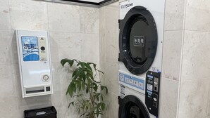 A public restroom with two washing machines, a trash bin, and a potted plant.