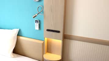 A hotel room with a bed, a bedside table with a lamp, a wall clock, and a telephone.