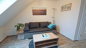 Una sala de estar moderna con un sofá gris, una mesa de centro de madera, una planta y un cuadro en la pared.