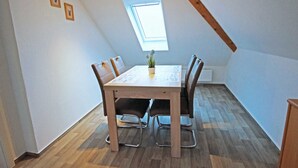 Comedor con mesa y sillas, un ventanal pequeño y suelo de madera.
