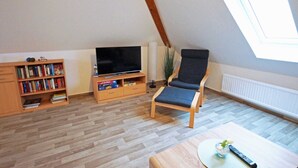 Una sala de estar con televisión, estantería y ventana.