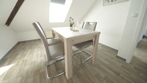 Ein Essbereich mit einem Holztisch, Metallstühlen, einer kleinen Topfpflanze und einem gerahmten Bild an der Wand.