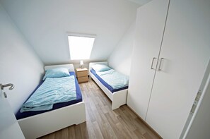 A small, well-lit room with two single beds, a nightstand, and a wardrobe.