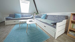 Ein Schlafzimmer im Loft-Stil mit hohen Decken, einem Oberlicht, einem weißen Sofa mit gemusterten Kissen, einem kleinen weißen Tisch und einem Bücherregal.