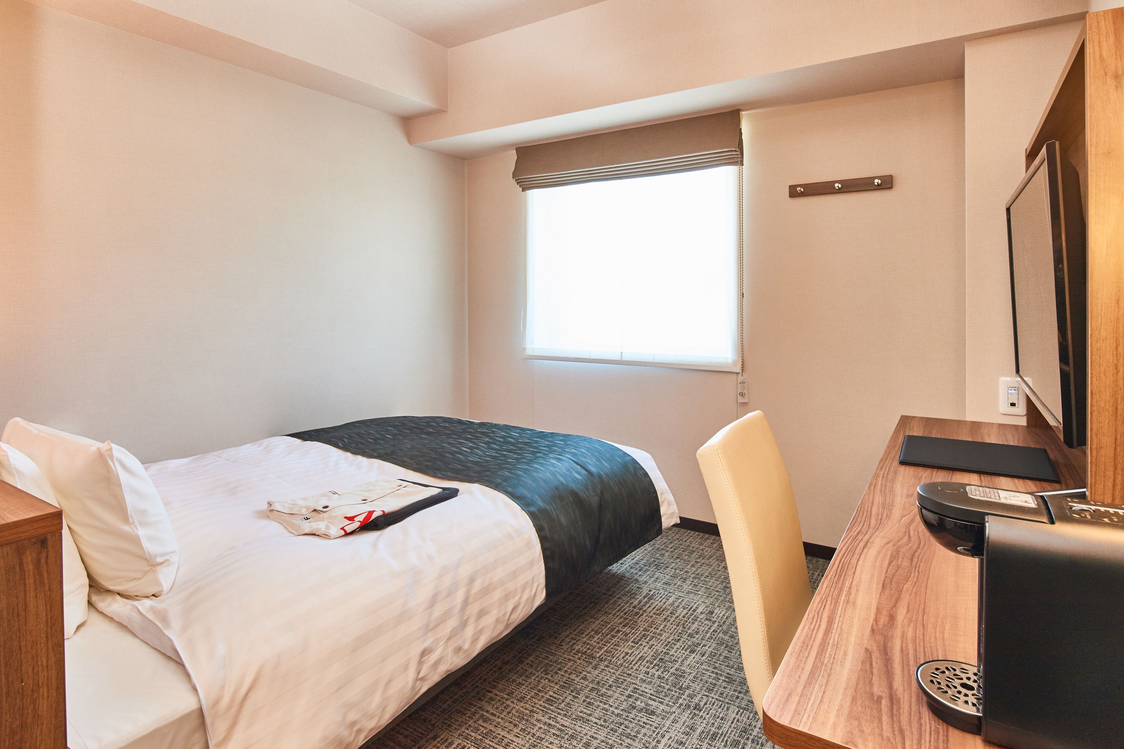 Habitación de hotel con cama, escritorio con computadora, ventana con persianas y televisor montado en la pared.