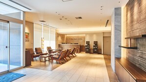 A modern hotel lobby with a reception desk, seating area, and a large wall with a textured design. - &and COMFY HOTEL Kumamotojo View (Kumamoto)