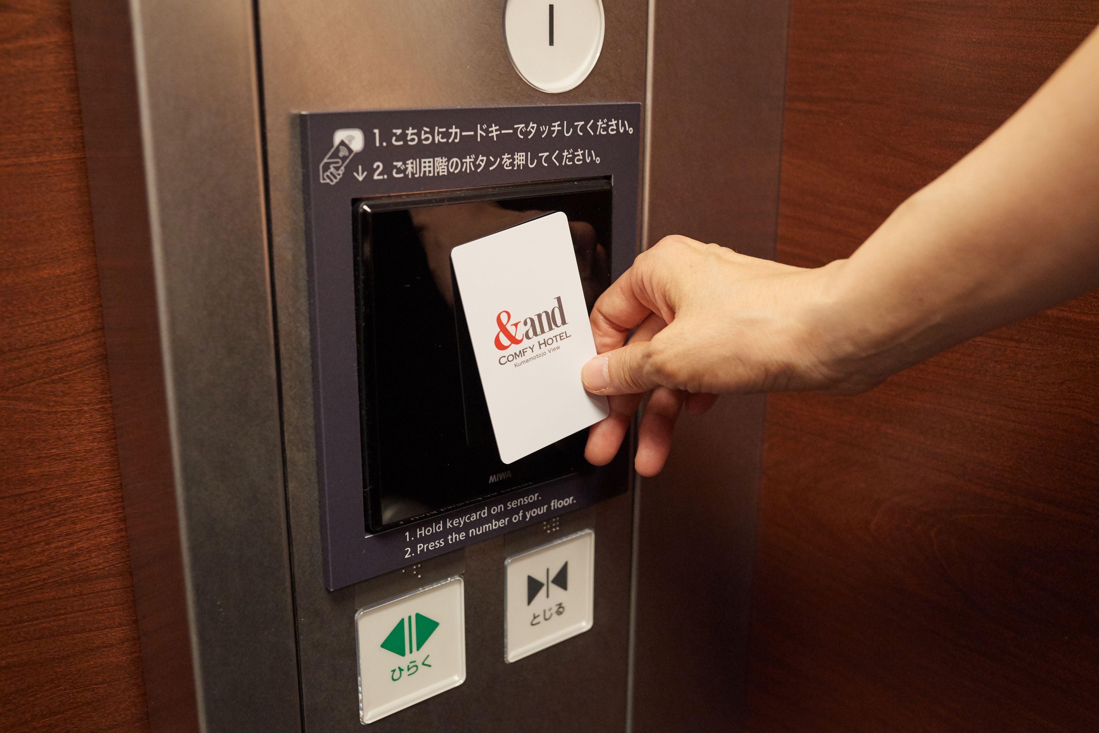 A hand inserting a card into an elevator card reader with instructions in Japanese.
