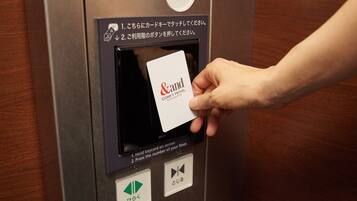 A hand inserting a card into an elevator card reader with instructions in Japanese.