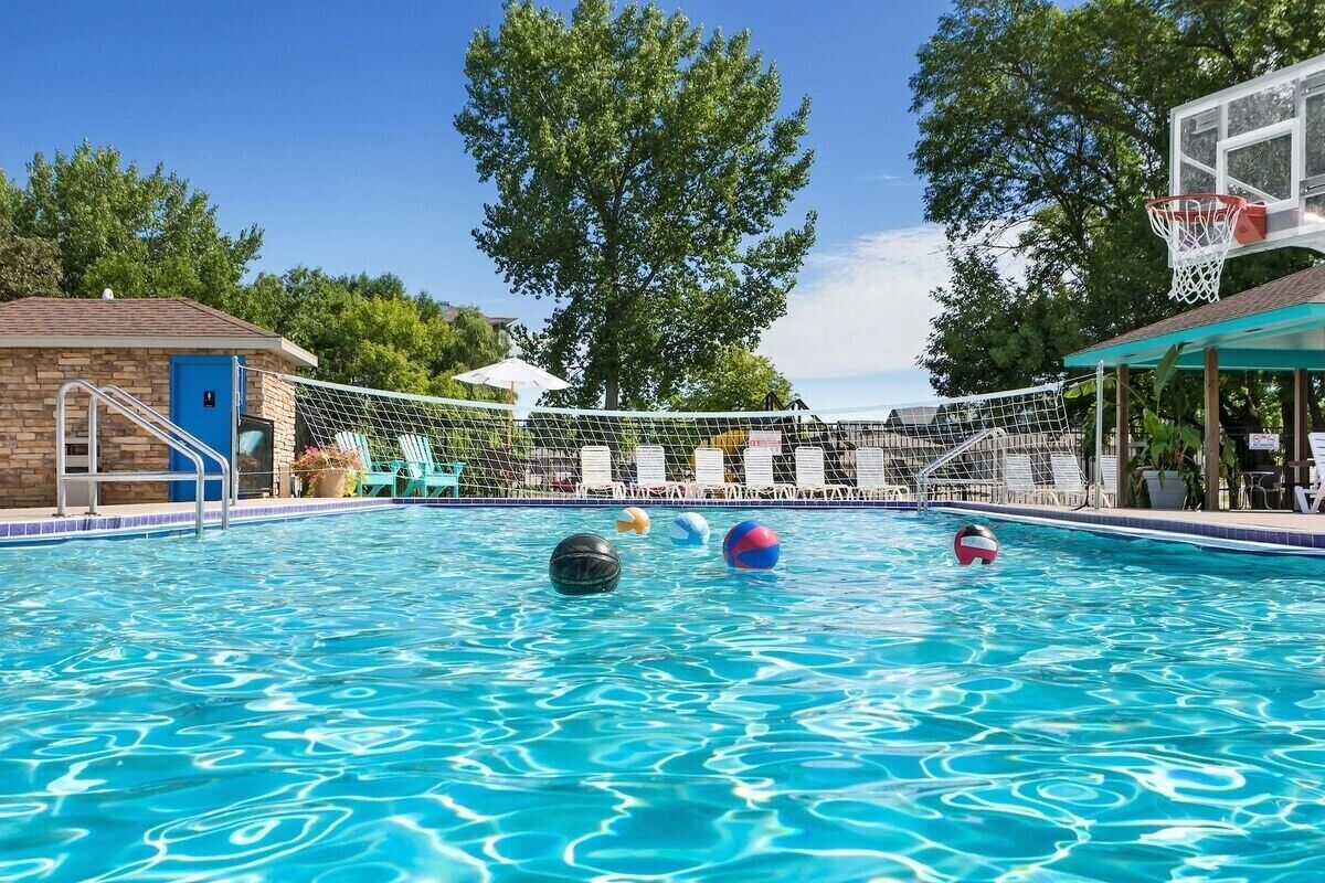 Piscina con una red de voleibol, sillas de descanso y un aro de baloncesto.