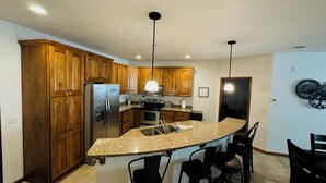A kitchen with wooden cabinets, a stainless steel refrigerator, a built-in oven, a microwave, and a granite countertop island with bar stools.