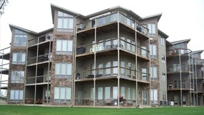 A multi-story building with balconies, large windows, and a grassy area in front.