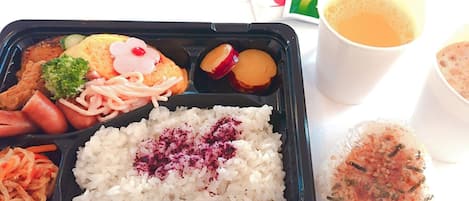 A bento box with rice, vegetables, and a drink.