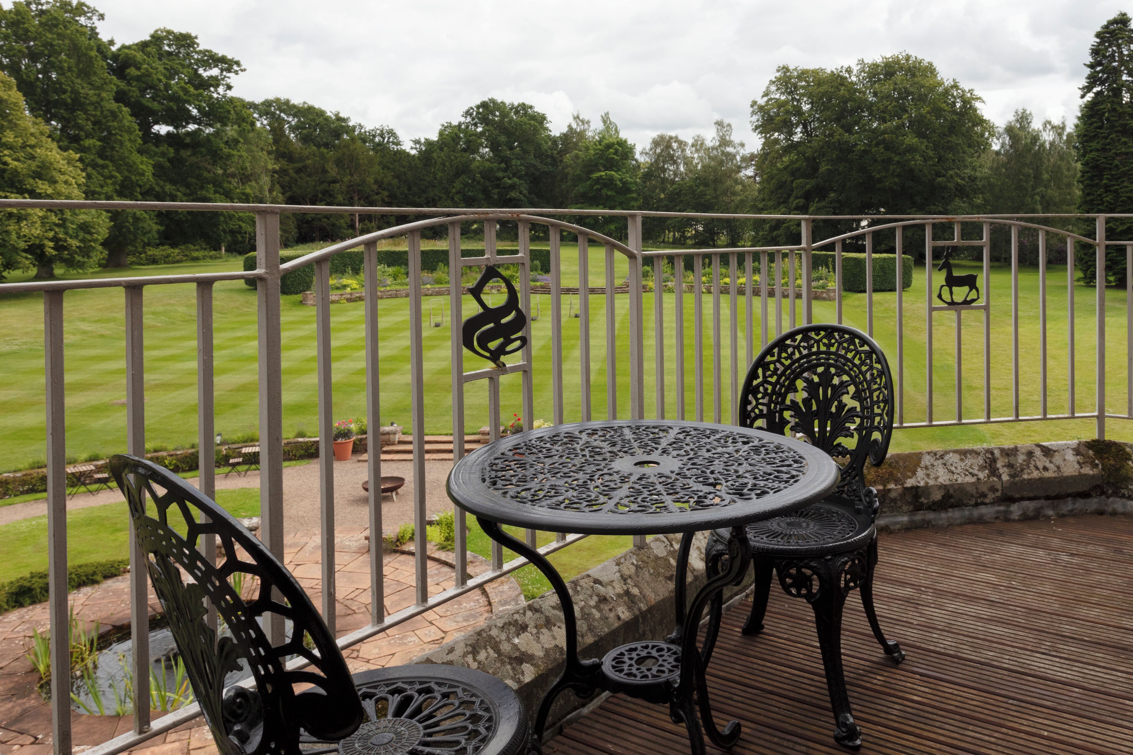 A patio with a round table and two chairs, overlooking a well-manicured lawn and trees.