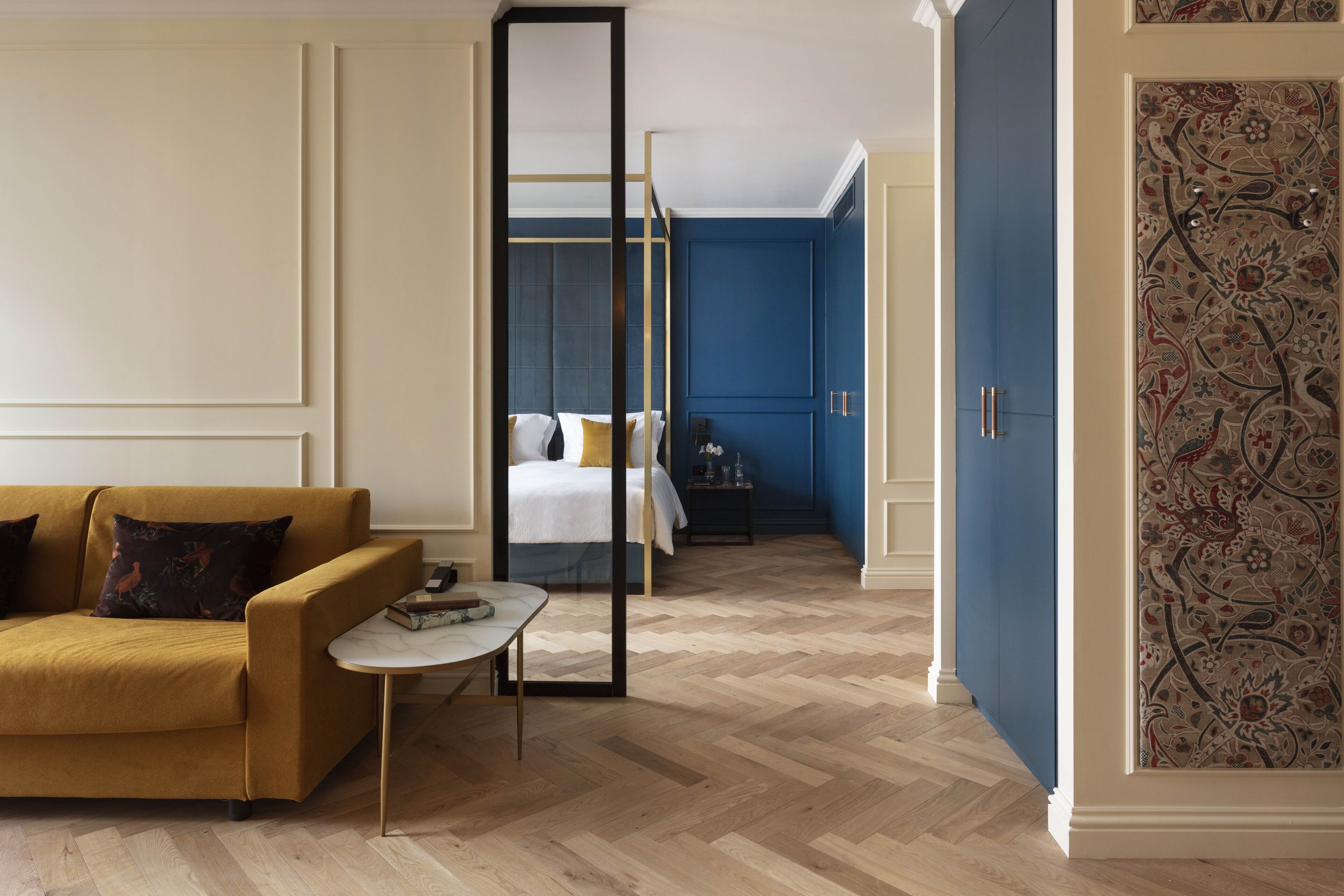 A hotel room with a sofa, a small table, a bed with a nightstand, and a blue accent wall.