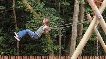 A person on a swing set in a wooded area.