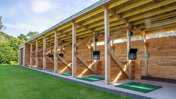 Una estructura de madera con techo inclinado, esteras verdes en el suelo y carteles informativos.
