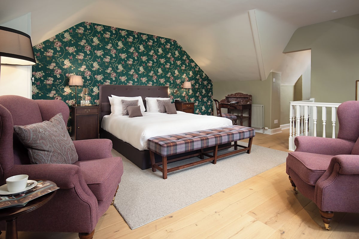 A bedroom with a large bed, two armchairs, a bench, and a nightstand.
