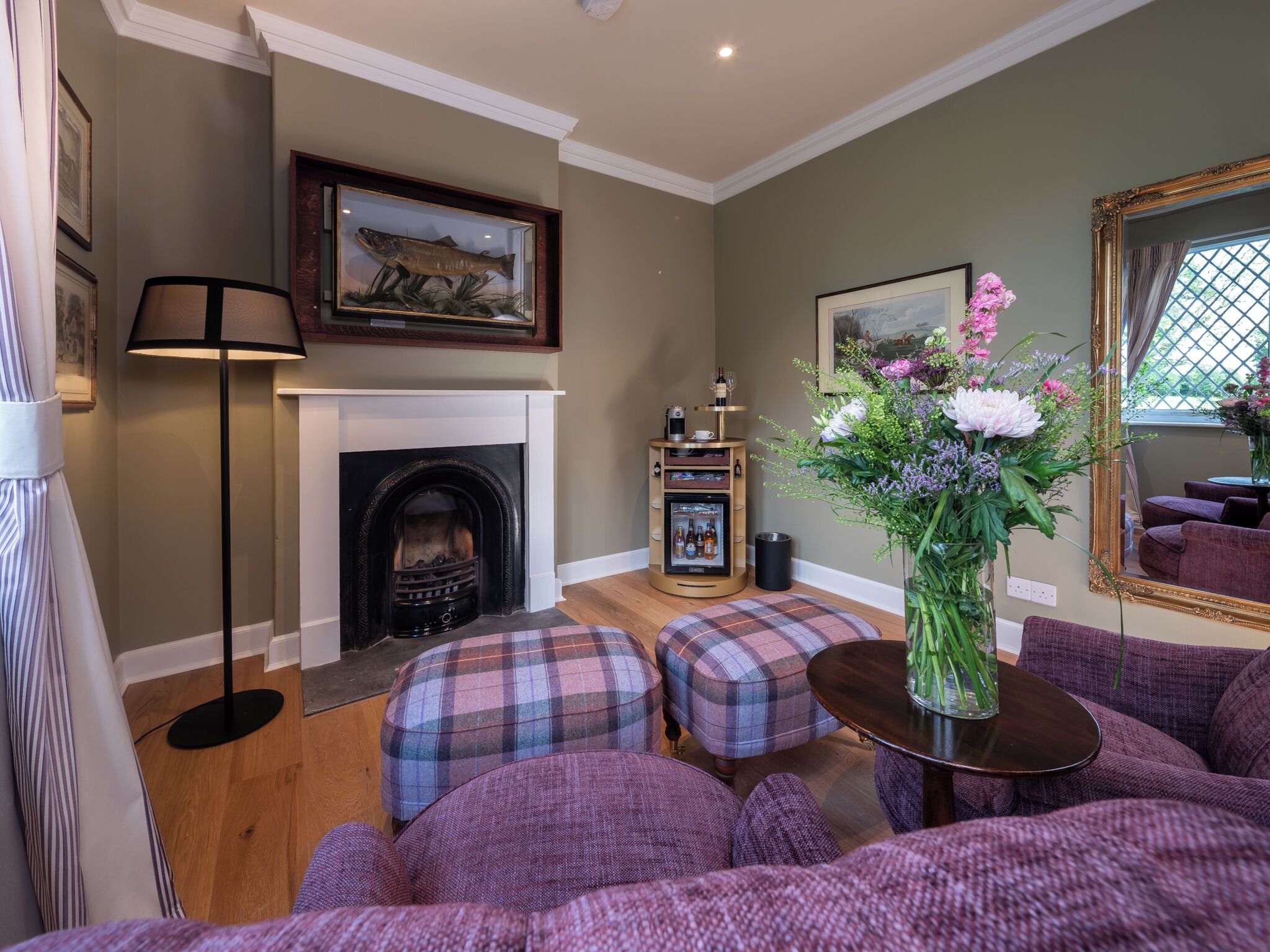 A cozy living room with a fireplace, plaid ottomans, a coffee table, and a vase of flowers.
