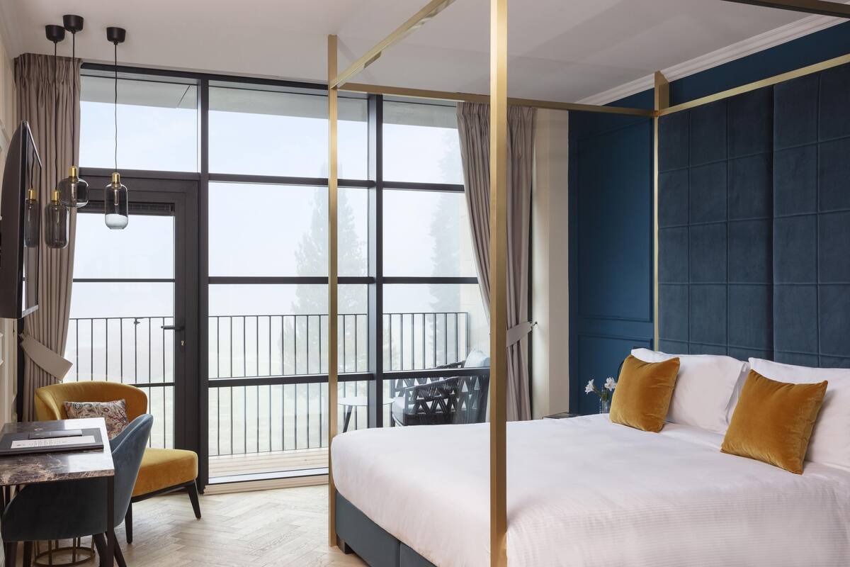 A modern hotel room with a large bed, a desk, and a balcony with outdoor furniture.