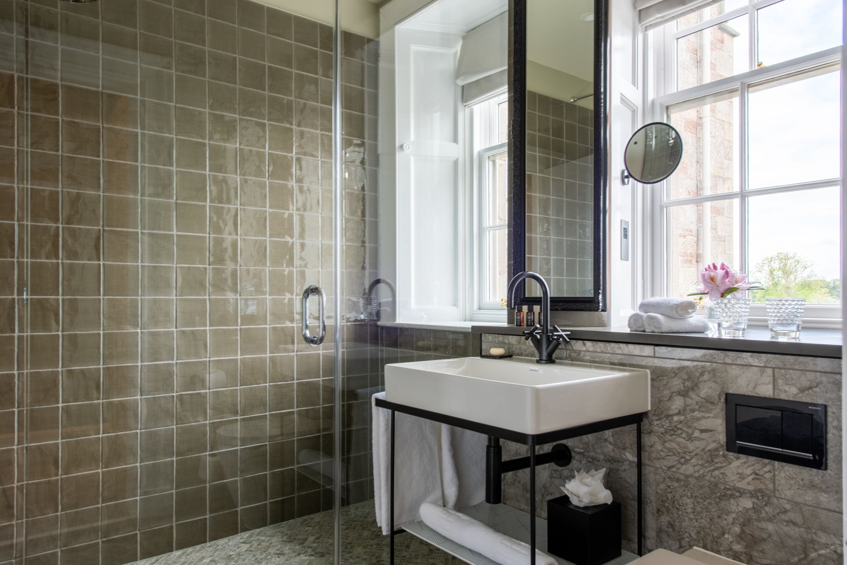 Un baño moderno con ducha de mampara de vidrio, lavamanos blanco y un espejo grande.