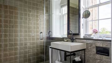 Un baño moderno con ducha de mampara de vidrio, lavamanos blanco y un espejo grande.