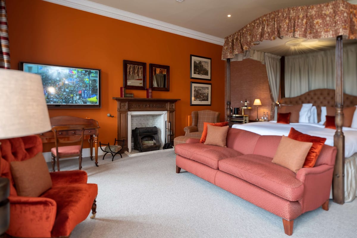 A hotel room with a fireplace, a large bed, a sofa, and a television.