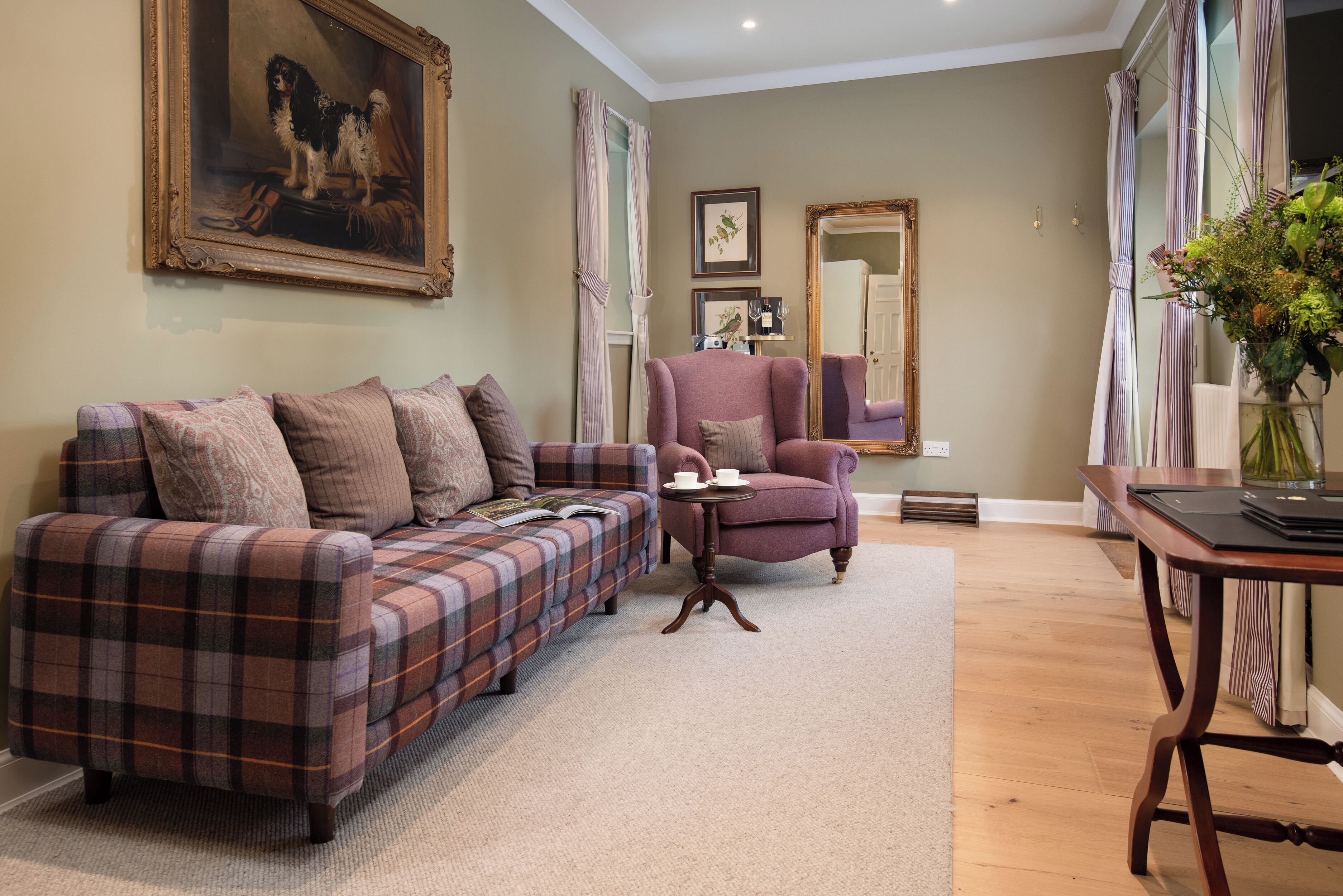 Un salon avec un canapé à carreaux, un fauteuil violet, une table basse en bois et un tableau accroché au mur.