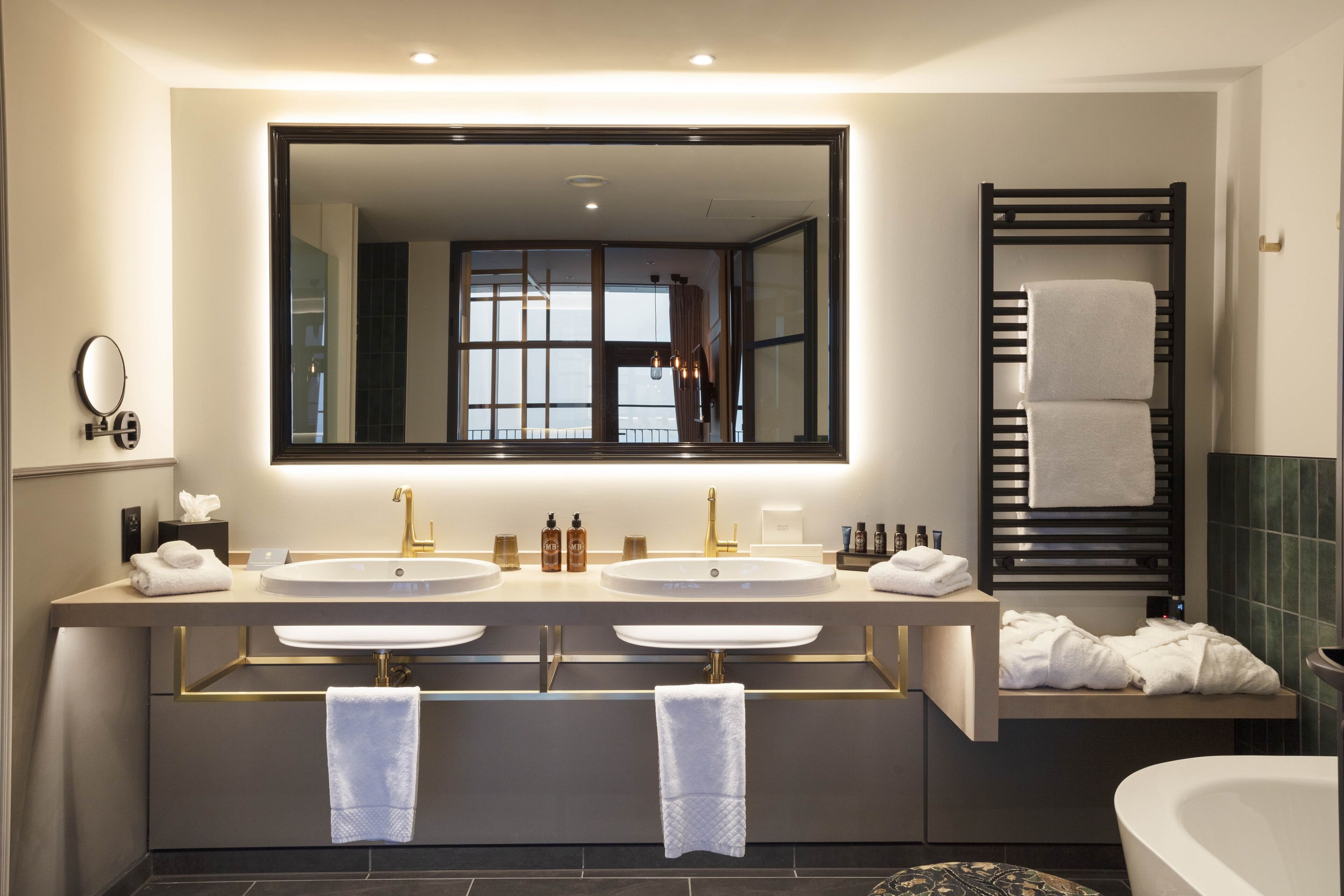 A modern bathroom with two sinks, a large mirror, and a bathtub.