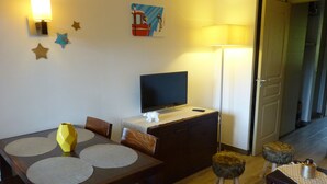 A dining area with a wooden table, chairs, a television, and a lamp. - BELLE PLAGNE, cosy 2 rooms, skis on / cleaning and covered parking included !!! (La Plagne Tarentaise)