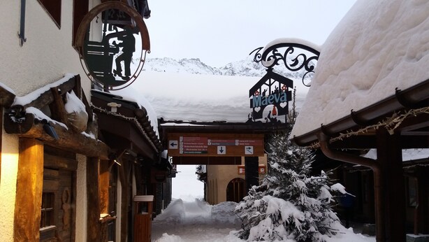 A snow-covered street with wooden buildings and a signboard. - BELLE PLAGNE, cosy 2 rooms, skis on / cleaning and covered parking included !!! (La Plagne Tarentaise)