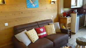 A cozy living room with a brown sofa, patterned cushions, a small wooden table, and a kitchen area in the background. - BELLE PLAGNE, cosy 2 rooms, skis on / cleaning and covered parking included !!! (La Plagne Tarentaise)