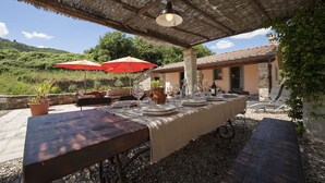 Un área de comedor al aire libre con una mesa larga dispuesta para una comida, rodeada de plantas en macetas y un techo rústico de paja.
