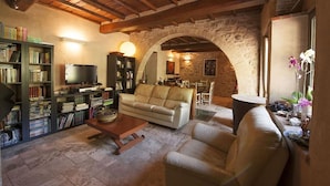 Una sala de estar acogedora con un arco de piedra, un sofá, una mesa de centro y estanterías con un televisor.