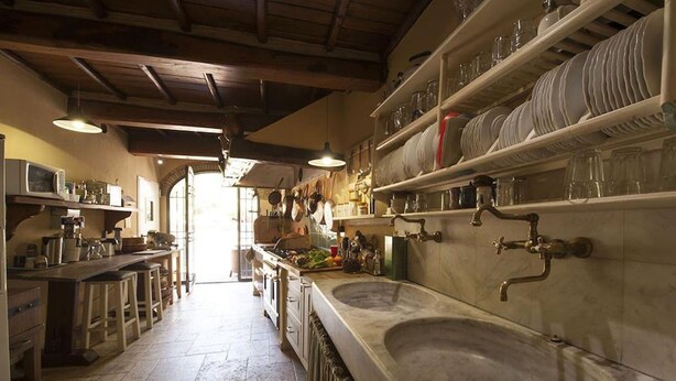 Una cocina con un lavamanos grande, estantes con vajilla y vistas al exterior.