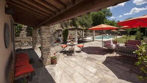 Un espacio al aire libre con piso de piedra, una piscina y sombrillas rojas.