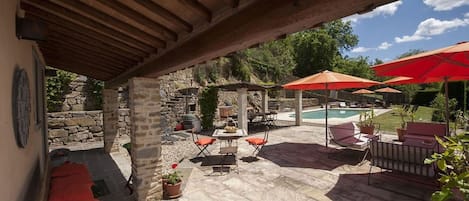 An outdoor patio area with stone flooring, a pool, and red umbrellas.